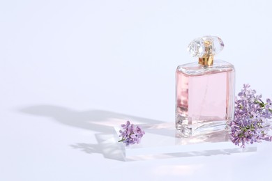 Photo of Bottle of perfume and lilac flowers on light grey background, closeup. Space for text
