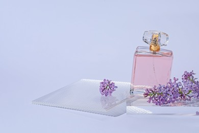 Photo of Stylish presentation of perfume bottle and lilac flowers on light grey background, closeup. Space for text