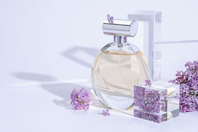 Photo of Stylish presentation of perfume bottle and lilac flowers on light grey background, closeup. Space for text