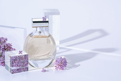 Photo of Stylish presentation of perfume bottle and lilac flowers on light grey background, closeup. Space for text
