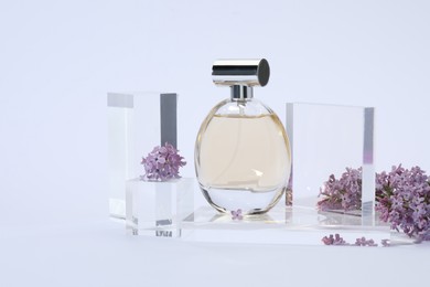 Photo of Stylish presentation of perfume bottle and lilac flowers on light grey background, closeup