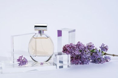 Photo of Stylish presentation of perfume bottle and lilac flowers on light grey background, closeup