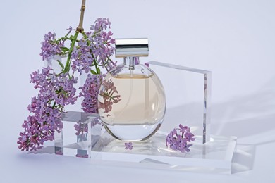 Photo of Stylish presentation of perfume bottle and lilac flowers on light grey background, closeup