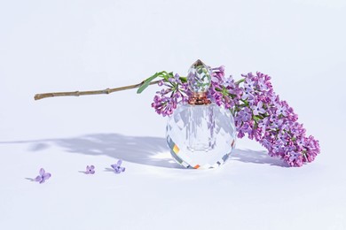 Photo of Perfume bottle and branch with lilac flowers on light grey background, closeup