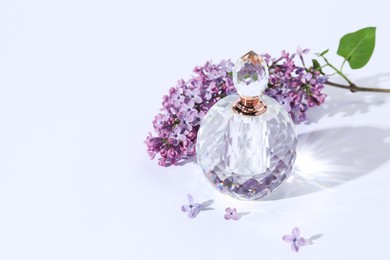 Photo of Perfume bottle and branch with lilac flowers on light grey background. Space for text