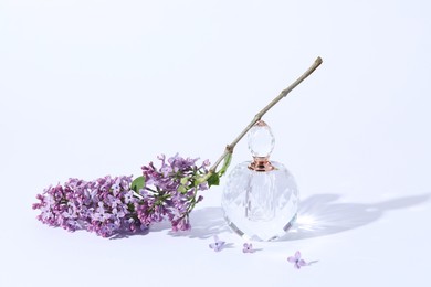 Photo of Perfume bottle and branch with lilac flowers on light grey background, closeup