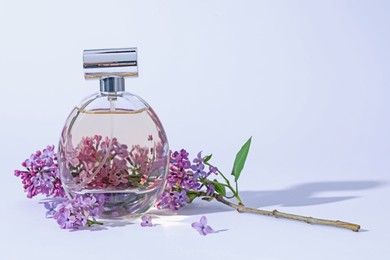 Photo of Perfume bottle and branch with lilac flowers on light grey background, closeup