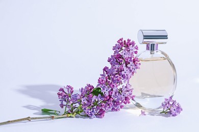 Photo of Perfume bottle and branch with lilac flowers on light grey background, closeup