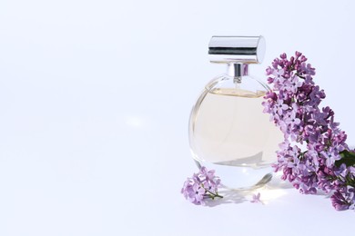 Photo of Perfume bottle and branch with lilac flowers on light grey background, closeup. Space for text