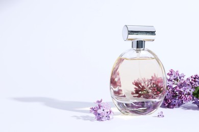 Photo of Perfume bottle and branch with lilac flowers on light grey background, closeup. Space for text