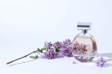 Photo of Perfume bottle and branch with lilac flowers on light grey background, closeup