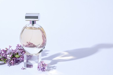 Photo of Perfume bottle and branch with lilac flowers on light grey background, closeup. Space for text