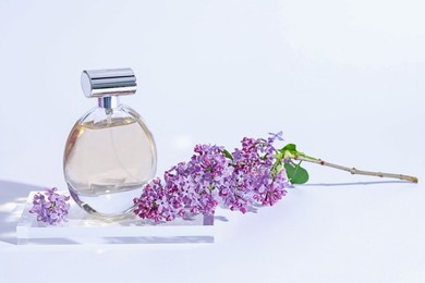 Photo of Perfume bottle and branch with lilac flowers on light grey background, closeup