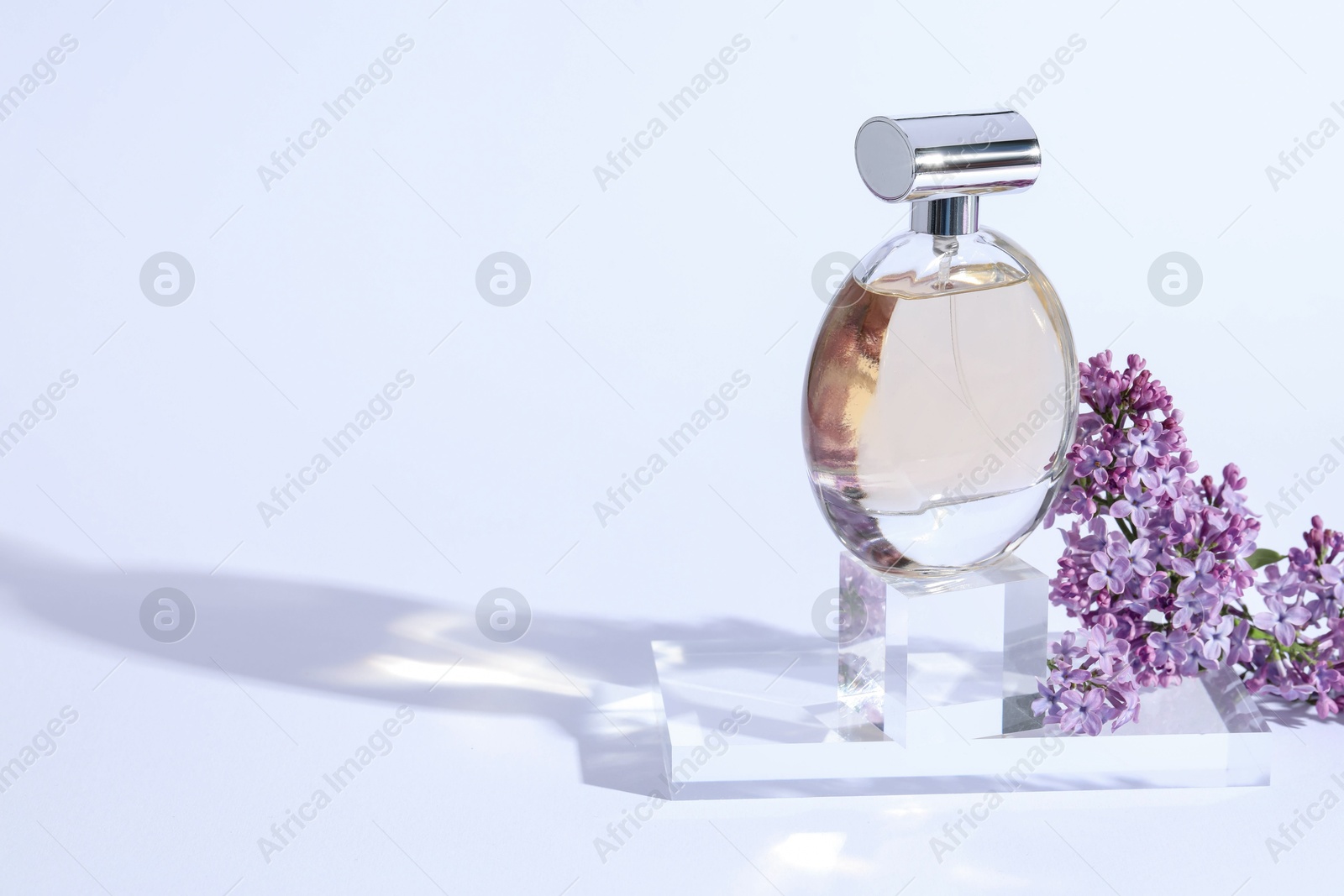 Perfume bottle and branch with lilac flowers on light grey background, closeup. Space for text Photo of Perfume bottle and branch with lilac flowers on light grey background, closeup. Space for text