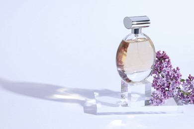 Photo of Perfume bottle and branch with lilac flowers on light grey background, closeup. Space for text