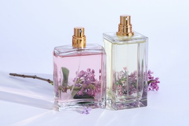 Photo of Perfume bottles and branch with lilac flowers on light grey background, closeup