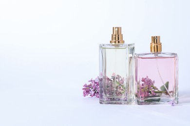 Photo of Perfume bottles and branch with lilac flowers on light grey background. Space for text
