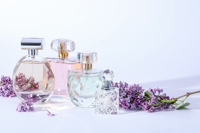 Photo of Perfume bottles and branches with lilac flowers on light grey background, closeup