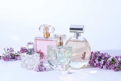 Photo of Perfume bottles and branches with lilac flowers on light grey background, closeup
