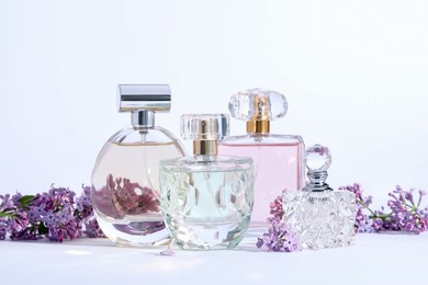 Photo of Perfume bottles and branches with lilac flowers on light grey background, closeup