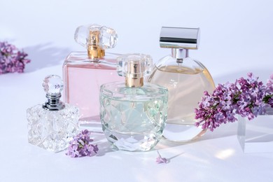 Photo of Perfume bottles and branches with lilac flowers on light grey background, closeup