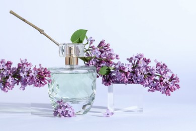 Photo of Perfume bottle and branches with lilac flowers on light grey background, closeup