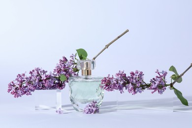 Photo of Perfume bottle and branches with lilac flowers on light grey background, closeup