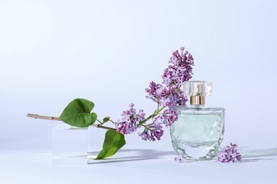 Photo of Perfume bottle and branch with lilac flowers on light grey background, closeup