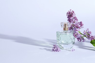 Photo of Perfume bottle and branch with lilac flowers on light grey background. Space for text