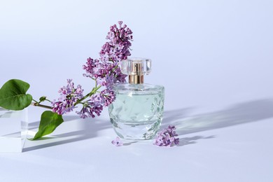 Photo of Perfume bottle and branch with lilac flowers on light grey background, closeup