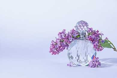Photo of Perfume bottle and branch with lilac flowers on light grey background, closeup. Space for text