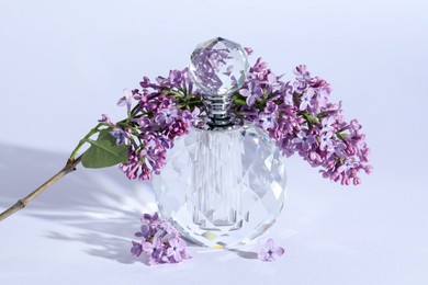 Photo of Perfume bottle and branch with lilac flowers on light grey background, closeup