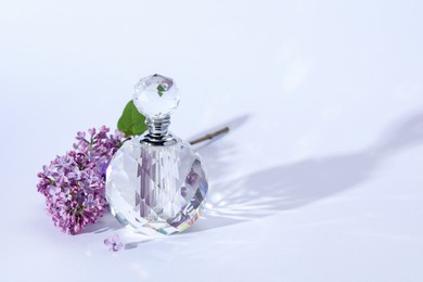 Photo of Perfume bottle and branch with lilac flowers on light grey background, closeup. Space for text