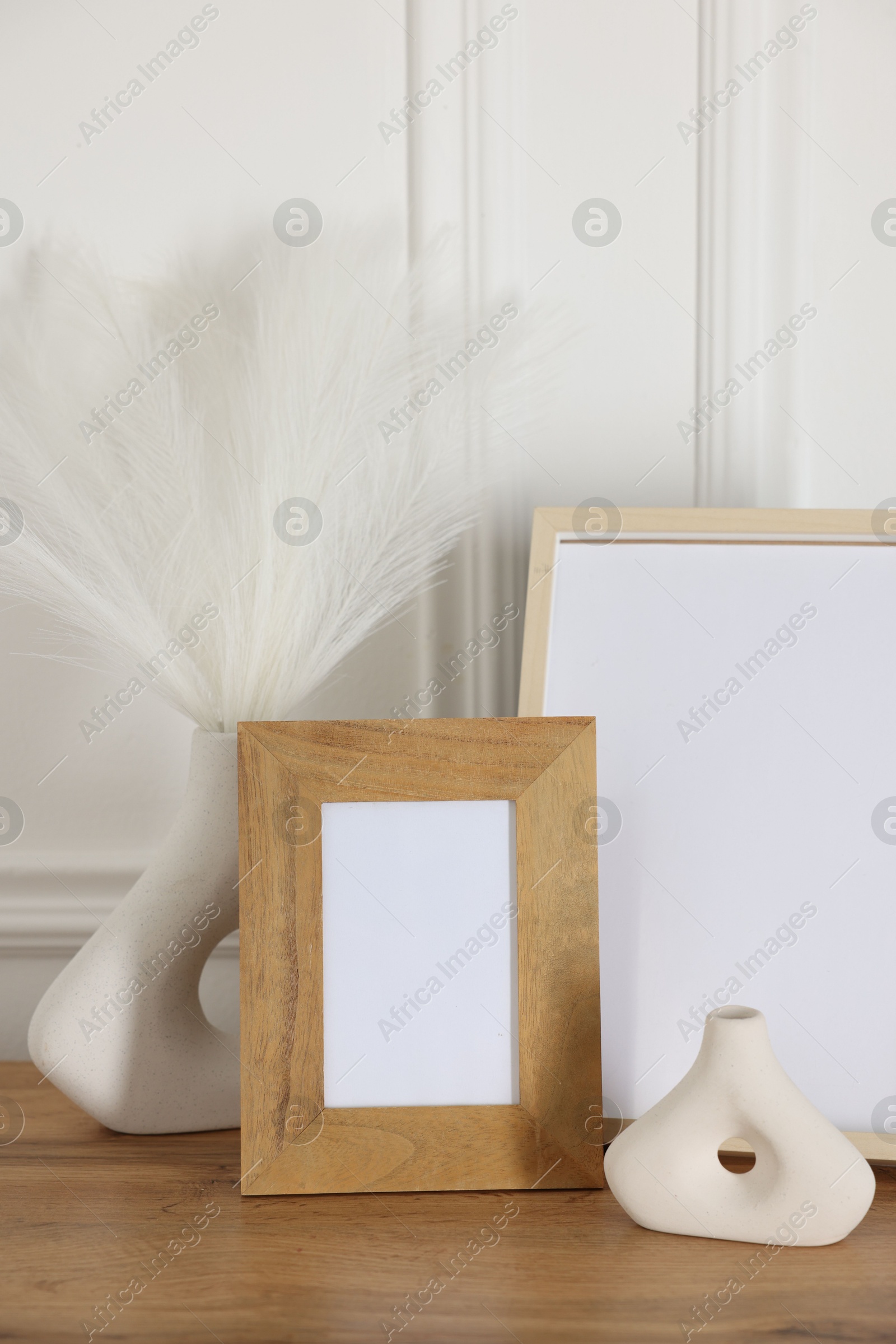 Empty photo frames and decor on wooden table near white wall Photo of Empty photo frames and decor on wooden table near white wall