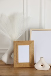 Photo of Empty photo frames and decor on wooden table near white wall