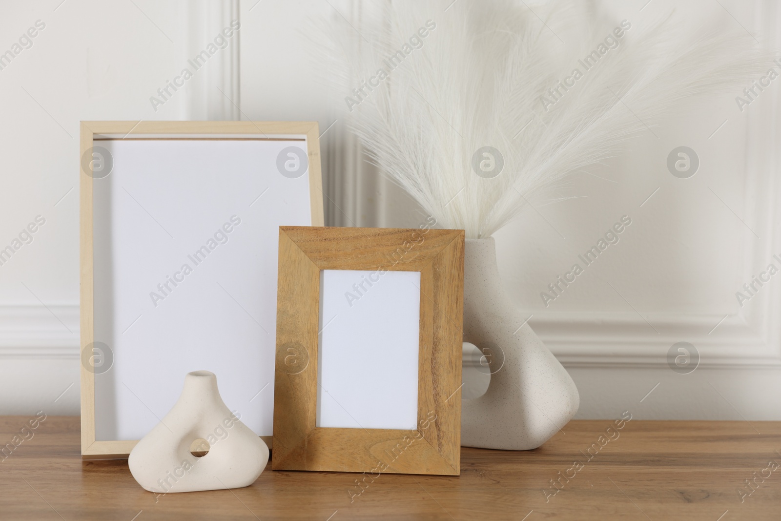 Empty photo frames and decor on wooden table near white wall Photo of Empty photo frames and decor on wooden table near white wall