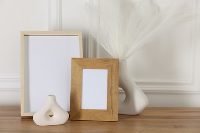 Photo of Empty photo frames and decor on wooden table near white wall