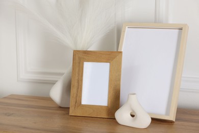 Photo of Empty photo frames and decor on wooden table near white wall