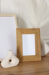Photo of Empty photo frames and decor on wooden table near white wall