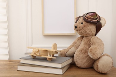 Photo of Teddy bear with vintage metal protective glasses, books and plane toy on wooden table