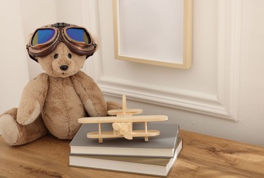 Photo of Teddy bear with vintage metal protective glasses, books and plane toy on wooden table. Space for text