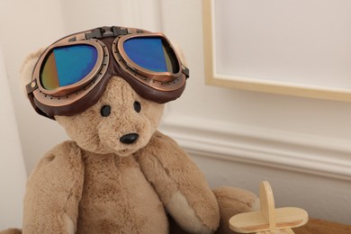Photo of Teddy bear with vintage metal protective glasses and plane toy on wooden table, closeup