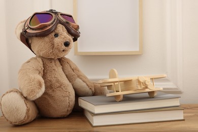 Photo of Teddy bear with vintage metal protective glasses, books and plane toy on wooden table