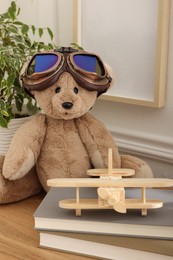 Photo of Teddy bear with vintage metal protective glasses, books and plane toy on wooden table