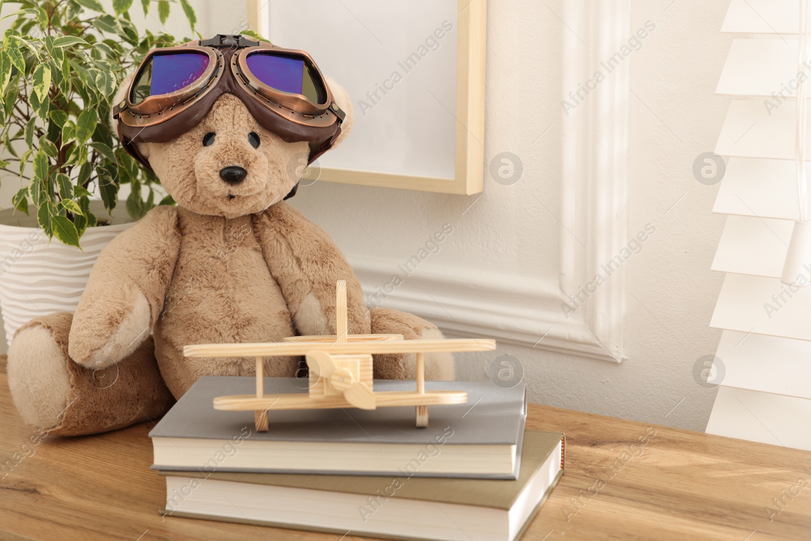 Teddy bear with vintage metal protective glasses, books and plane toy on wooden table. Space for text Photo of Teddy bear with vintage metal protective glasses, books and plane toy on wooden table. Space for text