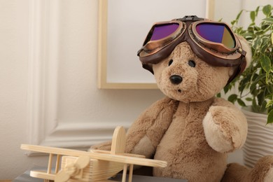 Photo of Teddy bear with vintage metal protective glasses and plane toy on table, closeup