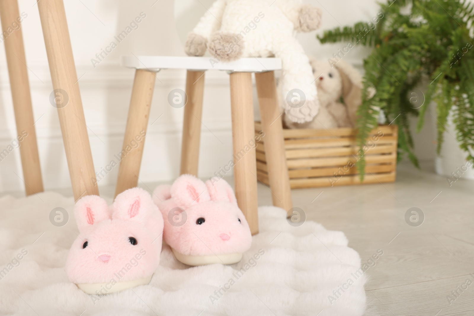Cute kid slippers in shape of bunnies on floor indoors, space for text Photo of Cute kid slippers in shape of bunnies on floor indoors, space for text