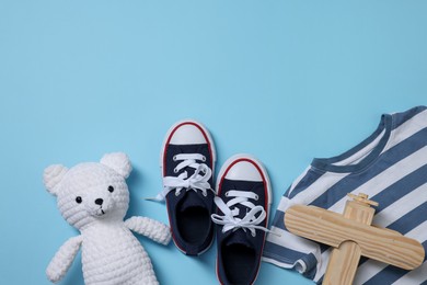 Photo of Teddy bear, wooden toy plane, shoes and t-shirt on light blue background, flat lay. Space for text