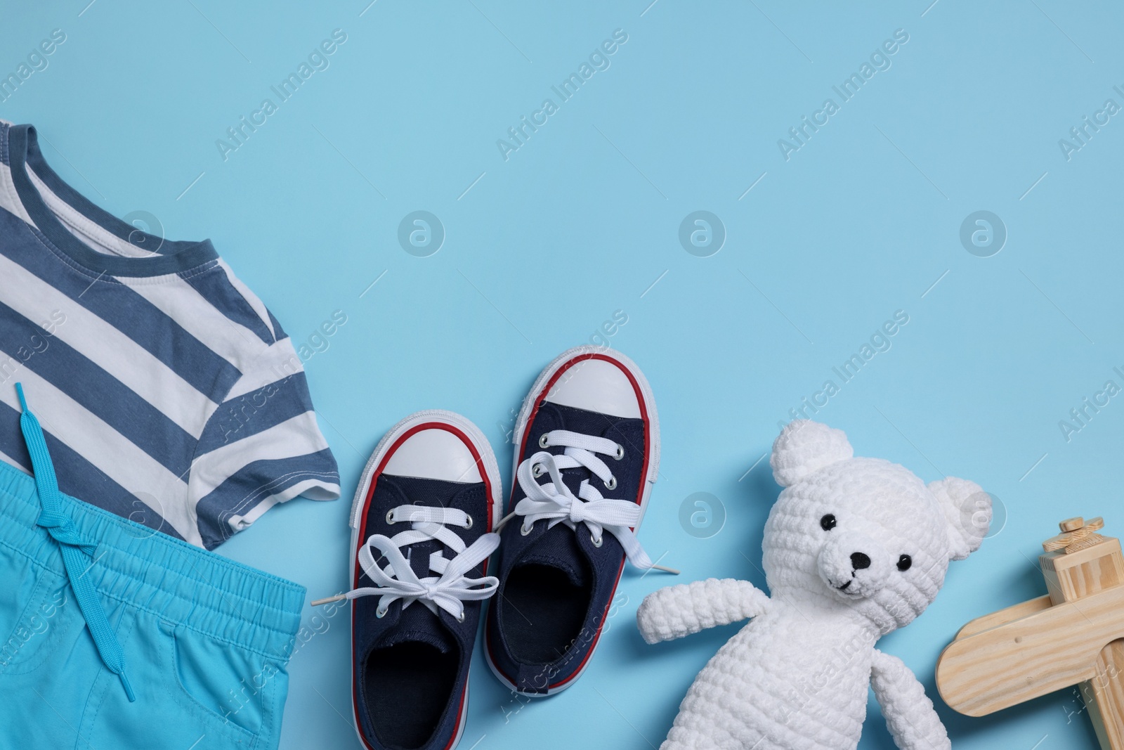 Teddy bear, wooden toy plane, shoes and t-shirt on light blue background, flat lay. Space for text Photo of Teddy bear, wooden toy plane, shoes and t-shirt on light blue background, flat lay. Space for text