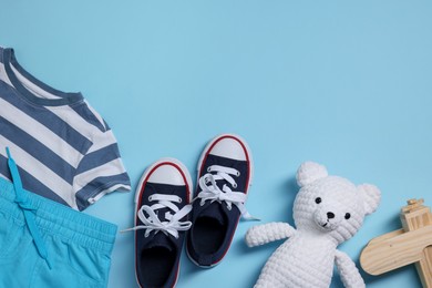 Photo of Teddy bear, wooden toy plane, shoes and t-shirt on light blue background, flat lay. Space for text